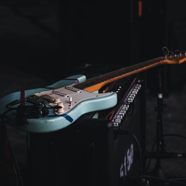 A blue rock guitar sitting on an amplifier.